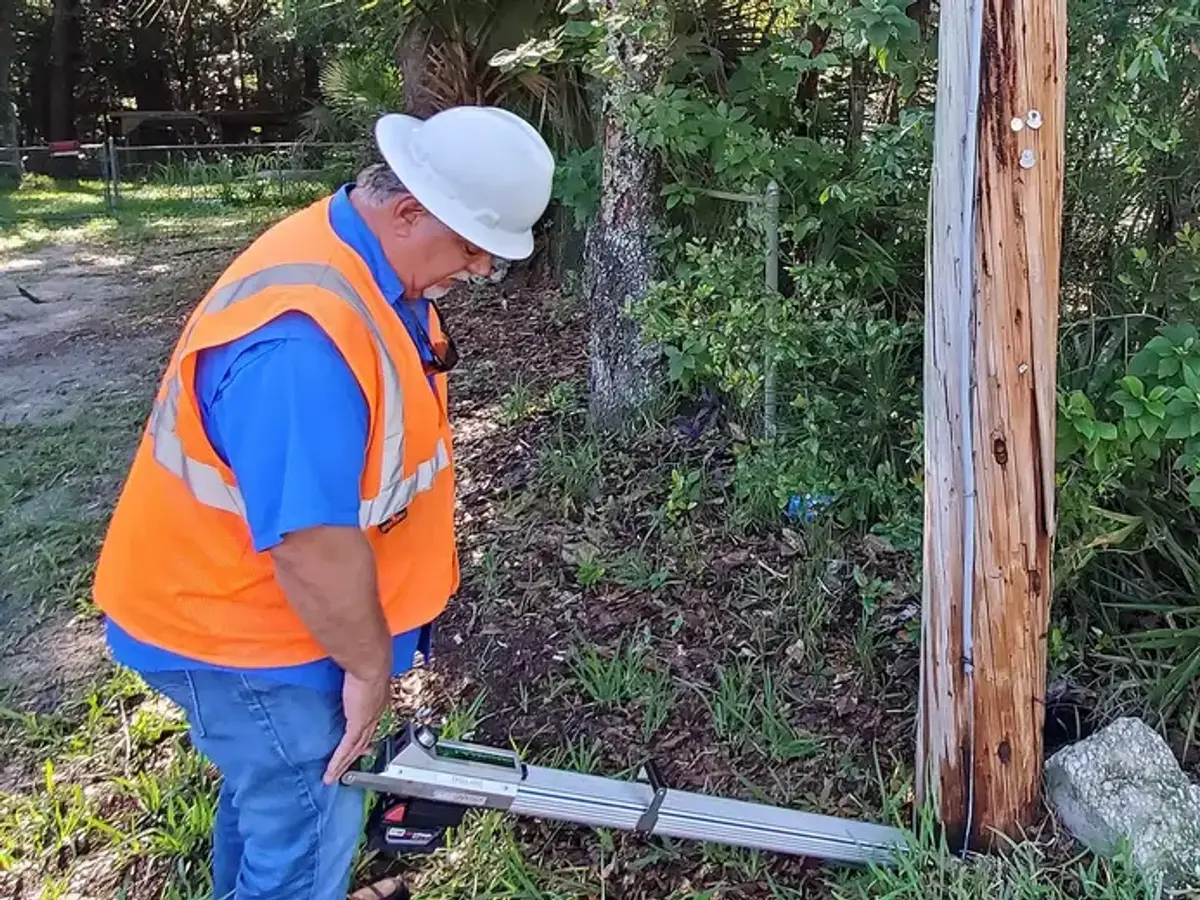 SPE inspector checking a distribution pole at ground line